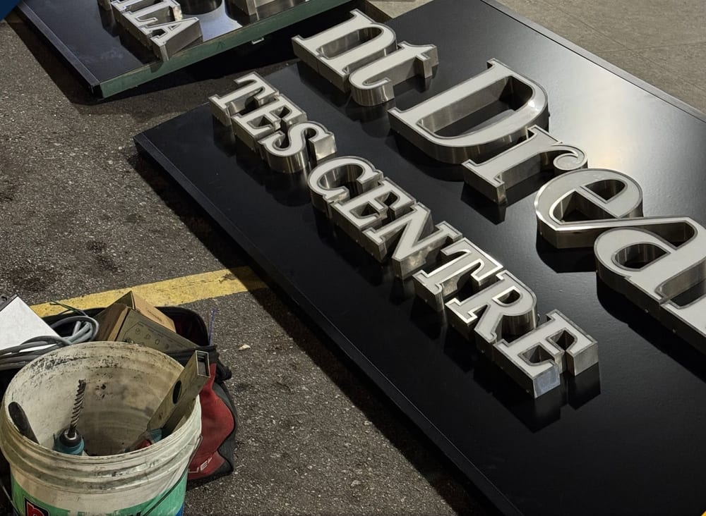 Cut metal letters laid out on the ground before mounting, standing proud of their backing plate.